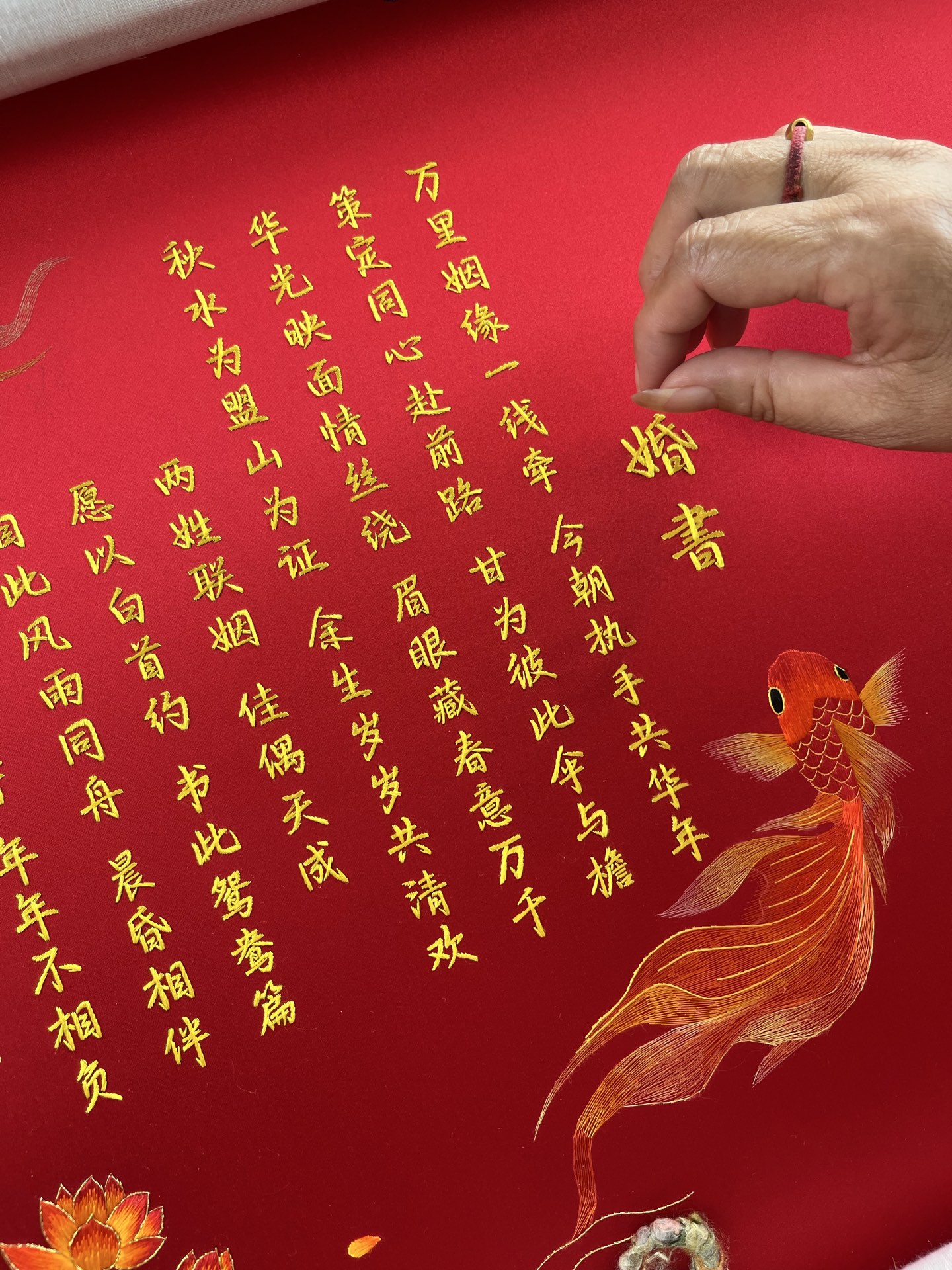 绣师在红色婚书绸面上绣制金色文字与锦鲤